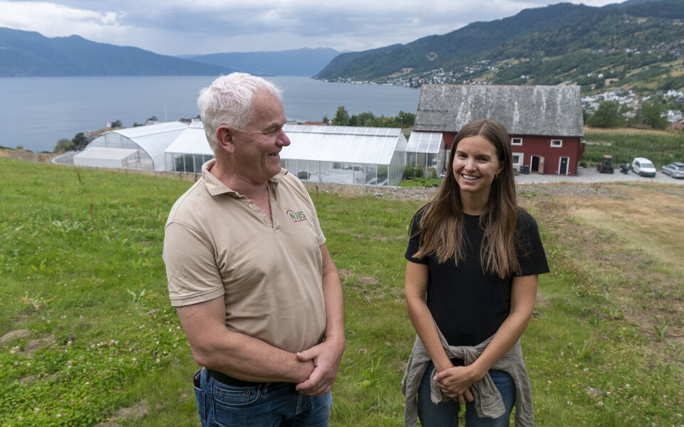 Stein Harald Hjeltnes og Kristina Alme Gardli med Njøs frukt- og bærsenter i bakgrunnen, vakkert beliggende i Leikanger i Sogndal.